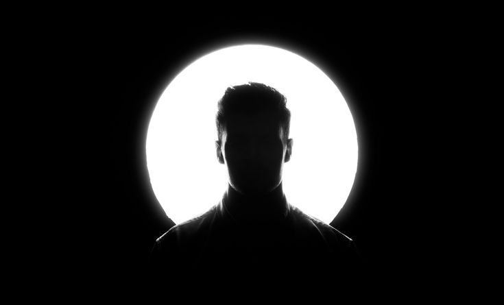 Silueta de una persona recortada contra un círculo de luz blanca.